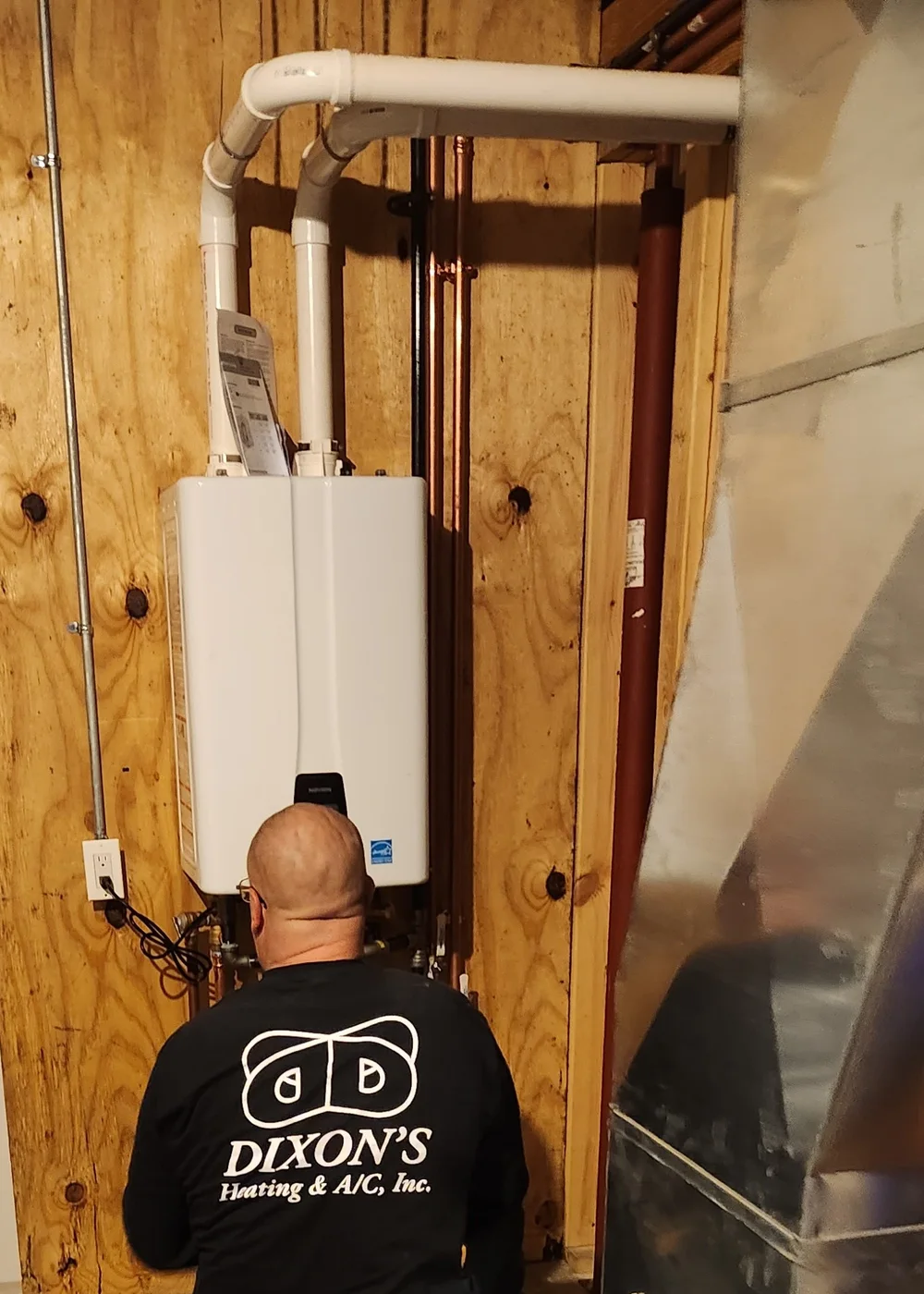 Dixon's technician working on indoor equipment while wearing a Dixon's Heating & Air Conditioning shirt.