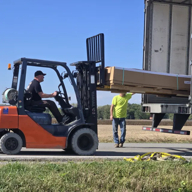 Dixon's lead tech on a Toyota forklift unloading crated stock from a semi-trailer on a rural Illinois highway